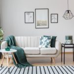 Black table next to sofa with green blanket in cozy apartment interior with gallery of posters